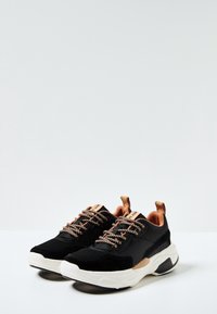 Černé a hnědé tenisky mají kombinaci síťoviny a semišového materiálu, s texturovanými tkaničkami a silnou bílou podrážkou. Jsou doplněny hnědými detaily.