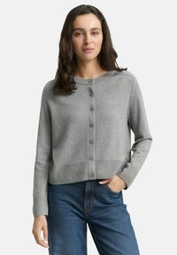 Grau gestrickte Strickjacke mit rundem Halsausschnitt, Knopfverschluss vorne sowie geripptem Saum und Bündchen. Tragen über blauem Denim-Jeans.