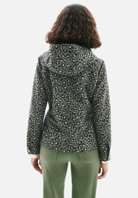 Veste imprimé léopard verte, en tissu léger, avec une capuche, des poches avant et des poignets à boutons. Associée à un pantalon vert.