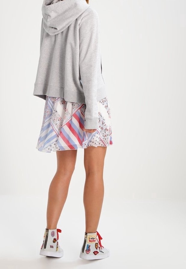 Sudadera gris con un corte relajado, capucha, combinada con una falda de patrón multicolor que presenta rayas y diseños florales, y zapatillas blancas.