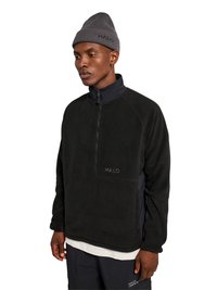 Ung mand iført en sort fleece med halv lynlås og "HALO"-logo, grå hue, hvid undertrøje og sorte bukser mod en hvid baggrund.