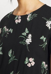 Mustat yläosat, joissa on vaaleanpunaisia ja vihreitä kukka- ja perhoskuvioita. Pehmeä rakenne, pyöreä pääntie ja lyhyet hihat.