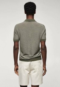 Polo shirt à manches courtes rayé vert avec un col assorti, associé à un short crème. Texture douce et design ajusté.