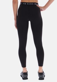 Czarne legginsy z wysokim stanem wykonane z elastycznego materiału, z markowym pasem i dopasowanym krojem, w połączeniu z czarnymi butami sportowymi.