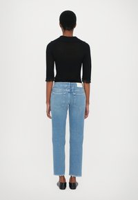 Top negro ajustado con mangas tres cuartos y bordes deshilachados; vaqueros de tiro alto azul claro con pierna recta y ligero deshilachado en los puños.