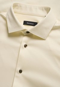 Krém színű ing, halszálka mintával, hegyes gallérral és sötétbarna gombokkal. A címkén ez áll: "Matinique."