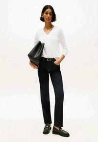 Haut blanc à manches longues en V, jeans droits bleu foncé, ceinture noire et mocassins noirs avec un sac à main noir texturé. Design simple.