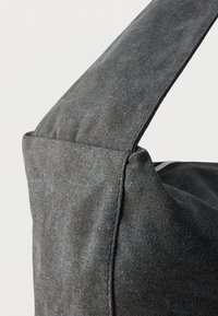 Szürke szövet táska strukturált kialakítással, hangsúlyos pánttal és finom textúrával. A varrás részletei láthatók a szélein.