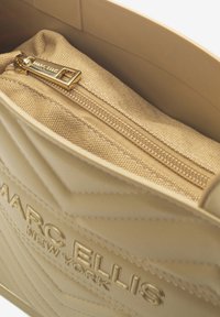Borsa beige con design trapuntato, dotata di zip dorata e fodera in tessuto. Nome del marchio "Marc Ellis" impresso all'esterno.
