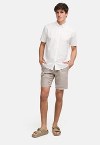 Cămașă albă cu mânecă scurtă, pantaloni scurți bej deschis și sandale verzi cu slip-on. Țesătura pare netedă, cu un design simplu și fără modele.