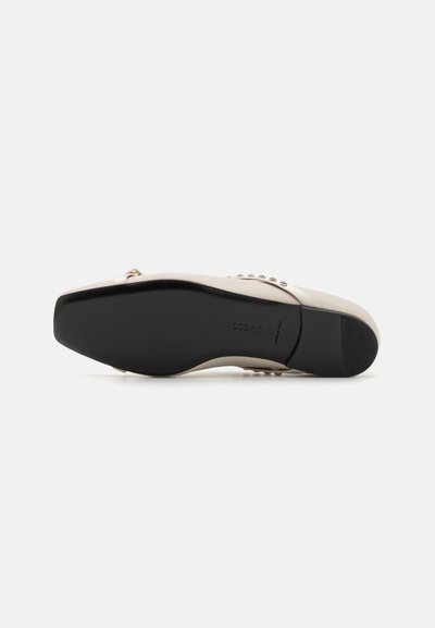 Chaussure à talon haut beige avec une tige lisse, ornée de clous en argent, et une semelle en caoutchouc noir solide, présentant une forme de chaussure arrondie.