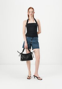 Top nero a halter, pantaloni shorts di jeans e sandali neri con tacco alto. Tiene una piccola borsa nera con parte superiore arricciata e finitura testurizzata.