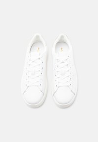 Paire de baskets basses blanches et propres avec des lacets blancs sur un fond gris clair uni, vues de dessus.