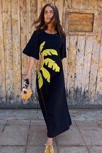 Zwarte jurk met bladerenpatronen in helder geel, korte mouwen, uitsnijding aan de zijkant, textiel fabric, gecombineerd met een beklede clutch en gele schoenen.