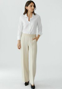 White button-up shirt and cream wide-leg trousers with a textured waistband and side pockets, paired with black pointed-toe heels.