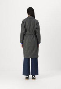 Grå ullfrakk med belted midje, lange ermer og krage, parret med vide denimbukser og joggesko.