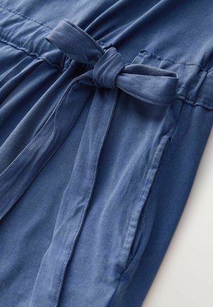 Rochie albastră din bumbac, cu cordon în talie, având o textură fină și buzunare laterale. Materialul se adună în talie pentru un fit lejer.