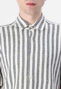 Camicia a button-up realizzata in tessuto testurizzato, caratterizzata da strisce verticali bianche e nere, un colletto e bottoni beige.