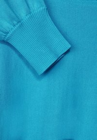 Turkos stickad tröja med ribbade muddar och en mjuk textur. Detaljerad sömnad längs sömmarna ger struktur åt designen.