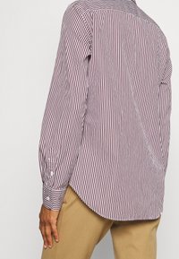 Camisa de manga larga con rayas verticales rojas y blancas, puños con botones y un dobladillo curvado. Fabricada con un tejido suave.