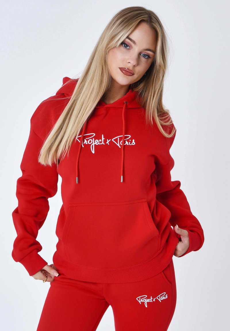 Felpa rossa con cappuccio e pantaloni coordinati in tessuto morbido, con un logo bianco "Project x Paris" sul davanti e sul lato. Il design include una tasca frontale e lacci.