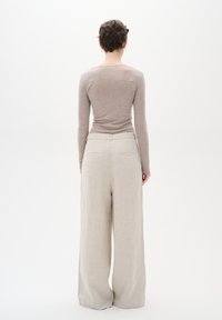 Maglietta lunga color marrone chiaro e pantaloni beige a gamba larga, realizzati in un tessuto morbido e con una superficie liscia. I pantaloni presentano due tasche posteriori.