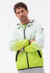 Giacca leggera con cappuccio, sfumata dal bianco al verde neon, dotata di una cerniera frontale e accenti e hardware neri a contrasto.