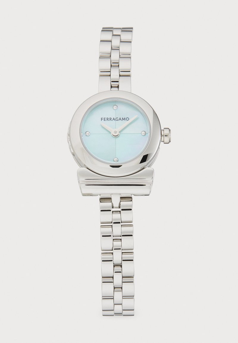 Sudraba metāla rokas pulkstenis ar apaļu seju, gaiši zilu ciparnīcu un četriem stundu rādītājiem. Iespējas ietver pulēta korpusa un minimālistisku dizainu.