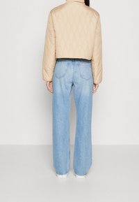 Beżowa pikowana krótka kurtka ze stojącym kołnierzem, zestawiona z jasnoniebieskimi dżinsami o szerokich nogawkach. Prosty design bez widocznych wzorów ani elementów metalowych.