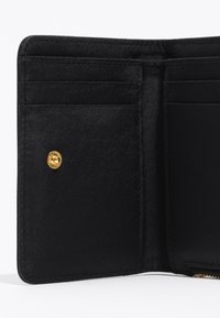 Interior de una cartera de tela negra con múltiples ranuras para tarjetas, textura suave y un botón de acento dorado. Diseño minimalista y forma suave.