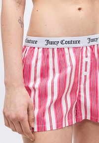 Μέση και χέρι ατόμου που φοράει ροζ και λευκά κατακόρυφα ριγέ μποξεράκια Juicy Couture με λογότυπο στη μέση και μικρό τατουάζ στο μπράτσο.