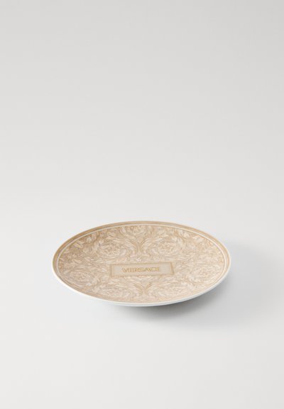 Okrągły ceramiczny talerz z beżowym kwiatowym wzorem i złotymi akcentami, z napisem „VERSACE” na środku. Gładka faktura, elegancki design.