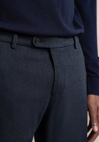 Marineblauwe textuurbroek met een subtiel patroon, voorzien van een sluiting aan de voorkant met een knoop en een tapered fit, aangevuld met een slanke tailleband.
