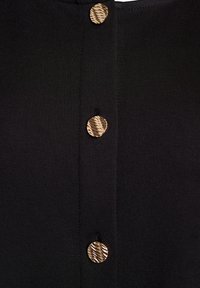 Svart tyg med en slät textur har tre knappar i guldton med ett randigt mönster ned längs mitten, vilket skapar en strukturerad design.