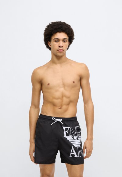 Čierne plavkové šortky s bielym logom, s elastickým pásom a šnúrkou na stiahnutie. Hladký, ľahký materiál; dizajn dĺžky po kolená.