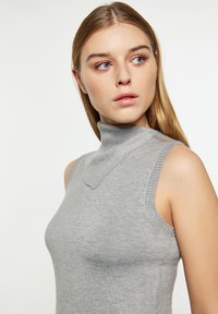 Maglione senza maniche grigio a collo alto, con un design aderente, una texture liscia e un distintivo dettaglio a scollatura a V.