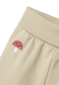 Beige Sweatpants mit einem gerippten Bund und einem bestickten pinken Pilzdesign an der Seite, mit einem weißen Stiel. Weiche Stofftextur.