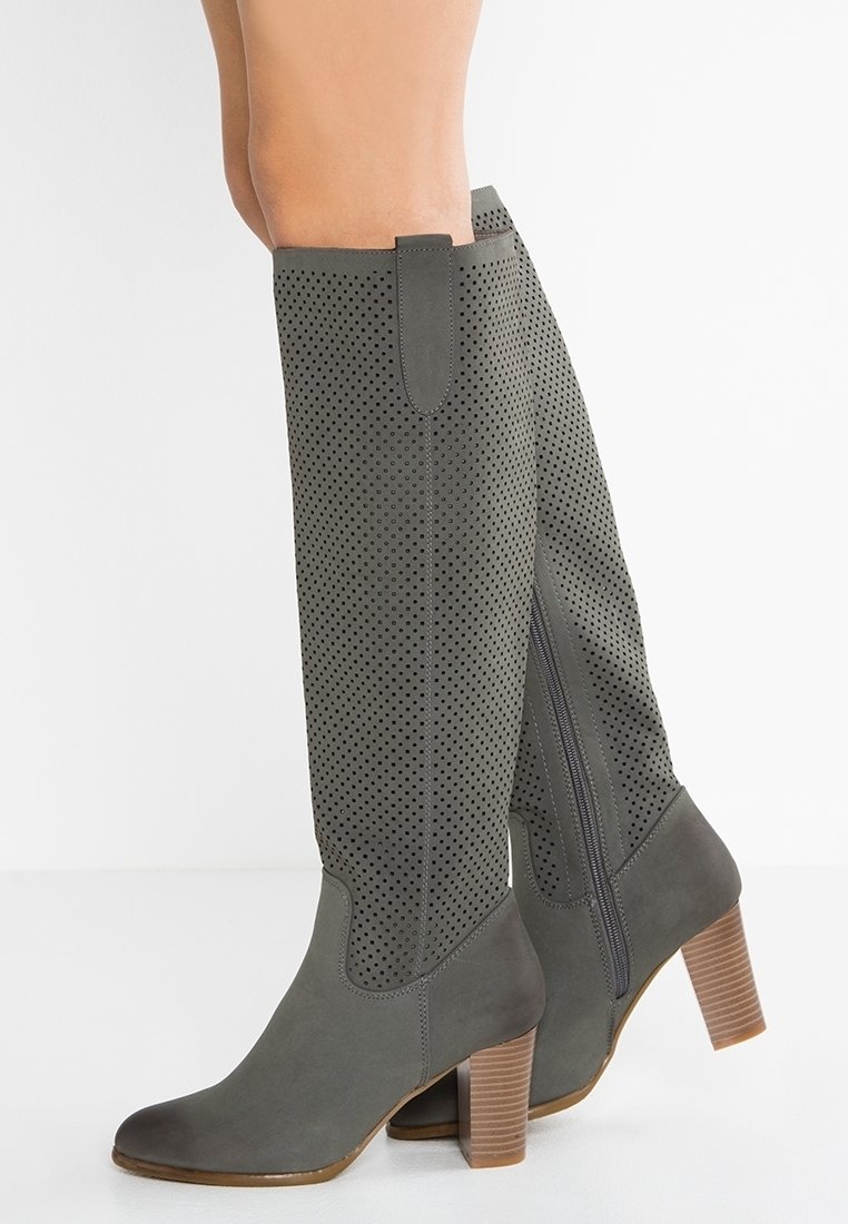 Bottes vertes en cuir perforé jusqu'au genou avec un talon bloc et une fermeture éclair latérale, présentant une texture lisse et un bout arrondi.