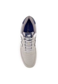 Scarpa sportiva grigia con tomaia liscia, design con lacci e dettagli blu navy. Presenta una superficie texturizzata e un logo sulla linguetta.