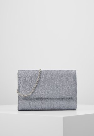 Zilveren glitter clutch met een klein gouden kettingbandje, rustend op een witte blok tegen een effen grijze achtergrond.