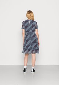 Mekko, jossa on laivastonsininen kuosi geometrisilla muodoilla, lyhyet hihat, röyhelöhelma ja avaus selkädetailina. Yhdistetty mustiin nilkkabootseihin.