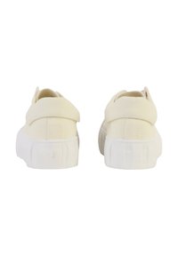 Cream-colored canvas shoes with a flat white sole, featuring a padded heel, rounded toe, and minimal stitching details.