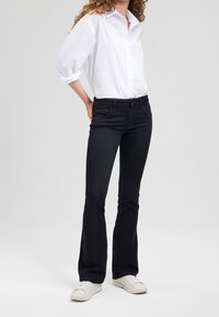 Mustat levenevät farkut keski- korkealla vyötäröllä, viisi taskua ja hienovarainen tekstuuri, yhdistettynä raikkaaseen valkoiseen nappipaitaan ja valkoisiin tennareihin.