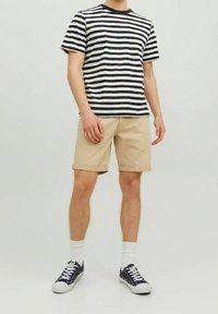 Pasiasta bawełniana koszulka w kolorze granatowym i kremowym, zestawiona z beżowymi szortami. Model ma na sobie białe skarpetki i granatowe sneakersy. Luźny krój, krótkie rękawy.