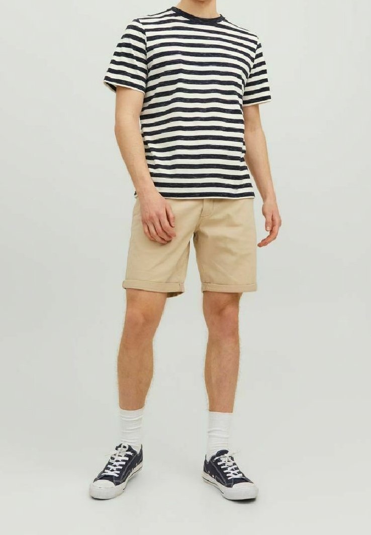 Pasiasta bawełniana koszulka w kolorze granatowym i kremowym, zestawiona z beżowymi szortami. Model ma na sobie białe skarpetki i granatowe sneakersy. Luźny krój, krótkie rękawy.