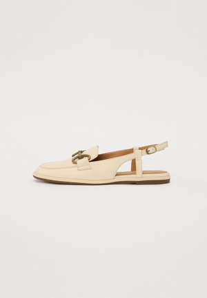 Chaussures à talon ouvert en cuir beige avec une semelle plate, ornées d'une boucle décorative et d'un design à bout fermé. Texture lisse et coutures minimales.