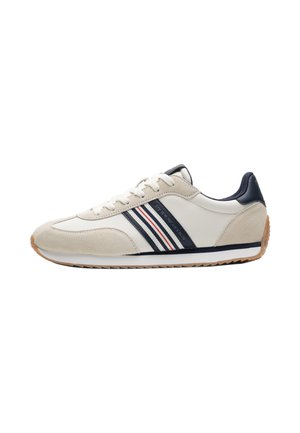 Crème en beige lage sneaker met marineblauwe accenten, witte veters, gestreept zijdetail en een rubberen zool, gezien vanaf de buitenkant.