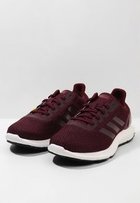 Burgundy urheilujuoksukengät, joissa on hengittävä verkkomateriaali, kolme raitaa logo, litteät nauhat, pehmustettu pohja ja musta pohja pitoon.