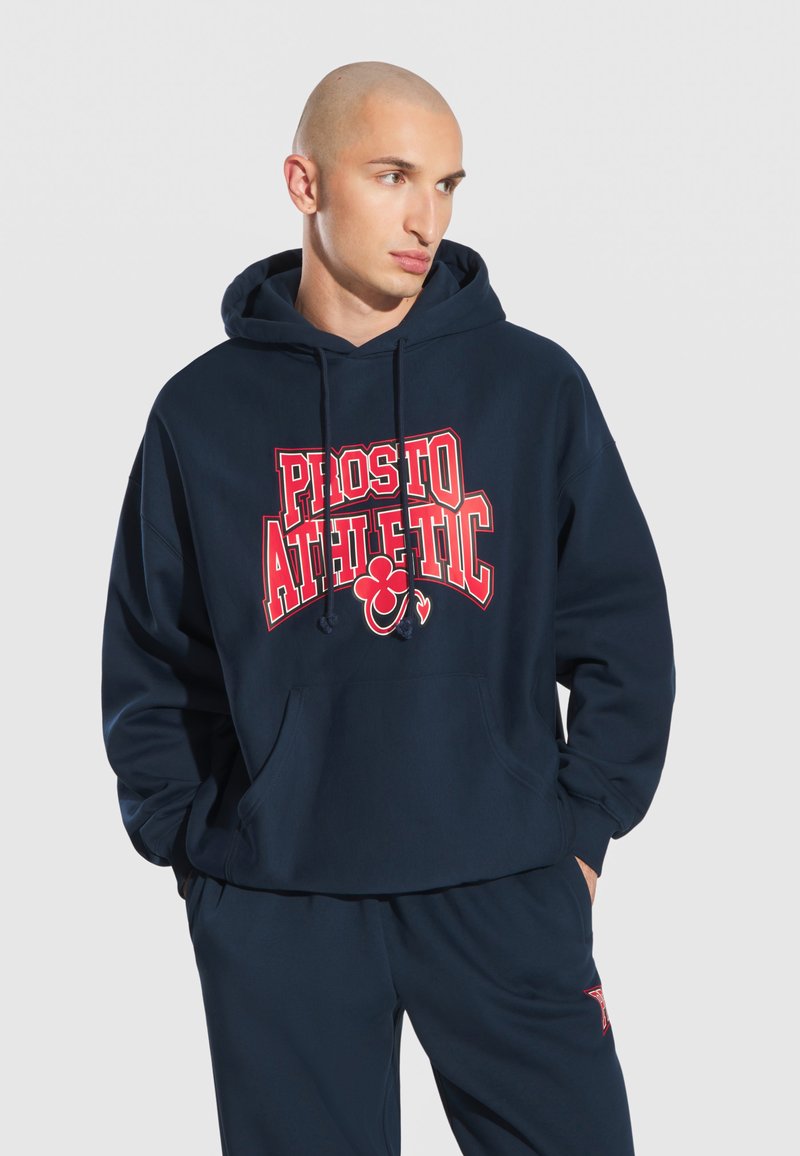 Granatowa bluza z kapturem wykonana z bawełny, z przednią kieszenią typu kangur, sznurkami ściągającymi oraz czerwonym napisem "PROSTO ATHLETIC" na klatce piersiowej.