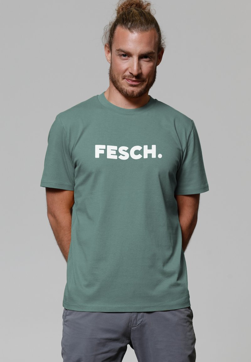 Mintgroene katoenen t-shirt met korte mouwen en een ronde halslijn, met opvallende witte tekst "FESCH." op de voorkant.